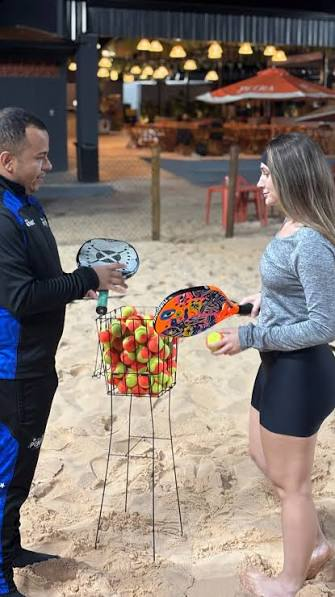 Professor e aluna com raquetes de beach tênis na areia